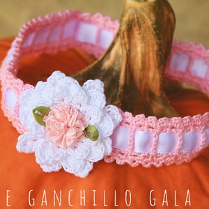 May include: A pink crocheted headband with a white crocheted flower and a pink satin ribbon. The headband is decorated with a white satin ribbon with pink squares.