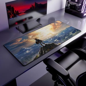 May include: A rectangular desk mat featuring a printed landscape illustration of a character standing on a rocky cliff overlooking a vast mountain range under a golden sunset sky with clouds, positioned on a dark gray desk surface.
