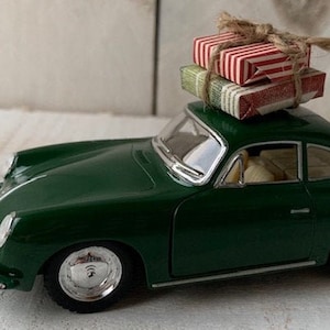 May include: A green toy car with a white roof and chrome wheels. The car is carrying two small, wrapped gifts on top.
