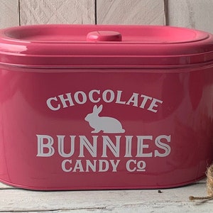 May include: Pink metal container with a white bunny and the text "Chocolate Bunnies Candy Co."
