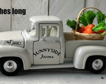 Puede incluir: Un camión de juguete blanco con una cesta de zanahorias en la caja. El camión mide 20,3 cm de largo y tiene escrito "Sunnyside Farms" en el lateral.