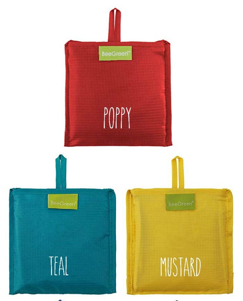 May include: Three reusable shopping bags in different colors: red, teal, and yellow. The bags are folded and have a handle. The bags have the words "BeeGreen" and "Poppy", "Teal", and "Mustard" printed on them.