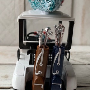 May include: A white golf cart with a blue and white Christmas tree on top. The cart has two golf bags, one brown and one blue, with golf clubs inside.
