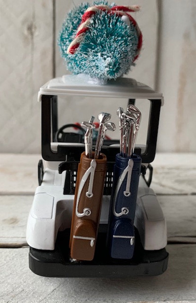 May include: A white golf cart with a blue and white Christmas tree on top. The cart has two golf bags, one brown and one blue, with golf clubs inside.