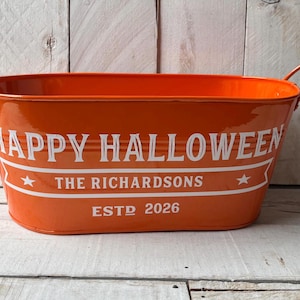 May include: An oval orange metal bucket with two side handles. The front features white text reading HAPPY HALLOWEEN, THE RICHARDSONS, and ESTD 2026, with two small white stars flanking the family name on a horizontal banner design.