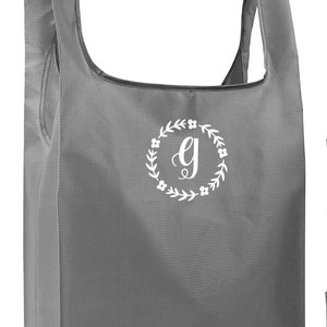 May include: A gray reusable shopping bag with a white floral wreath and the letter "G" in the center.