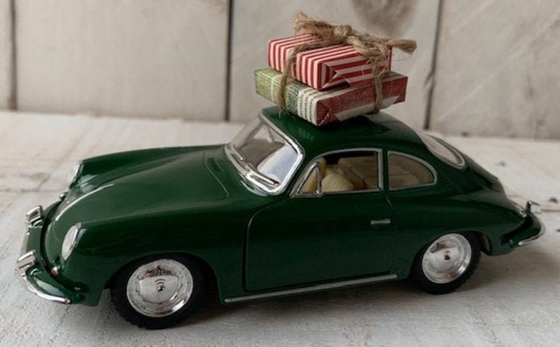 May include: A green toy car with a white roof and chrome wheels. The car is carrying two small, wrapped gifts on top.