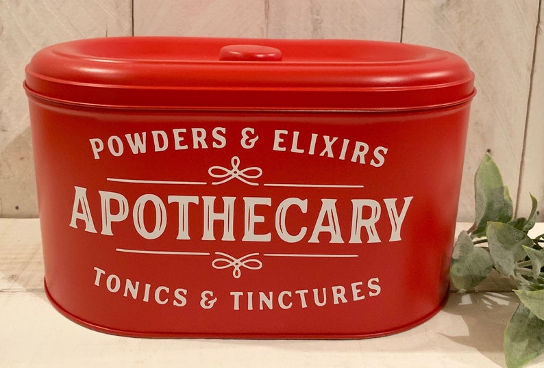 May include: Red metal canister with a white lid and white lettering that reads "POWDERS & ELIXIRS APOTHECARY TONICS & TINCTURES".