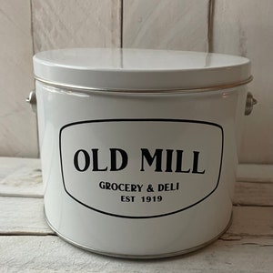 May include: White metal canister with a black oval label that reads "Old Mill Grocery & Deli Est 1919".