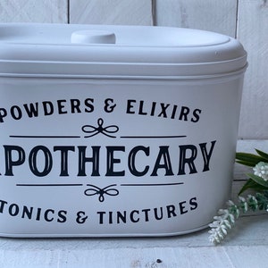 May include: White oval container with a black label that reads "POWDERS & ELIXIRS APOTHECARY TONICS & TINCTURES".