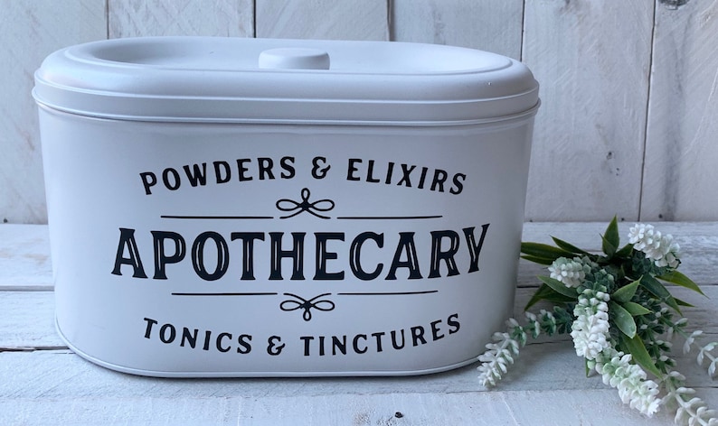 May include: White oval container with a black label that reads "POWDERS & ELIXIRS APOTHECARY TONICS & TINCTURES".