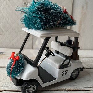 May include: A white golf cart with a black trim and a green Christmas tree on top. The cart has a number "22" on the side and a wreath on the front.