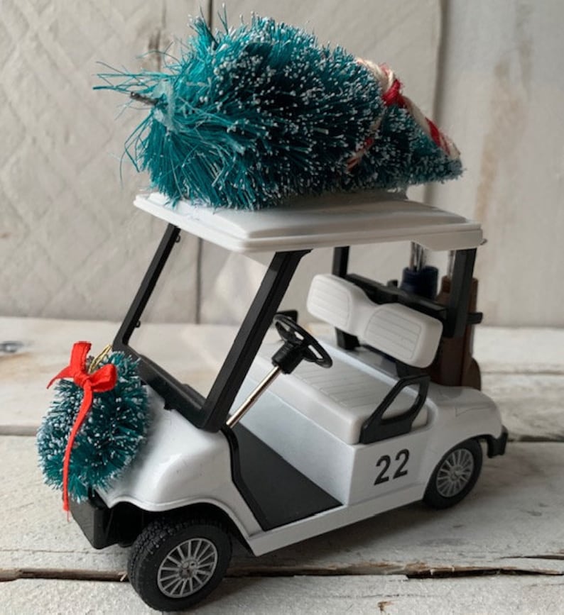 May include: A white golf cart with a black trim and a green Christmas tree on top. The cart has a number "22" on the side and a wreath on the front.