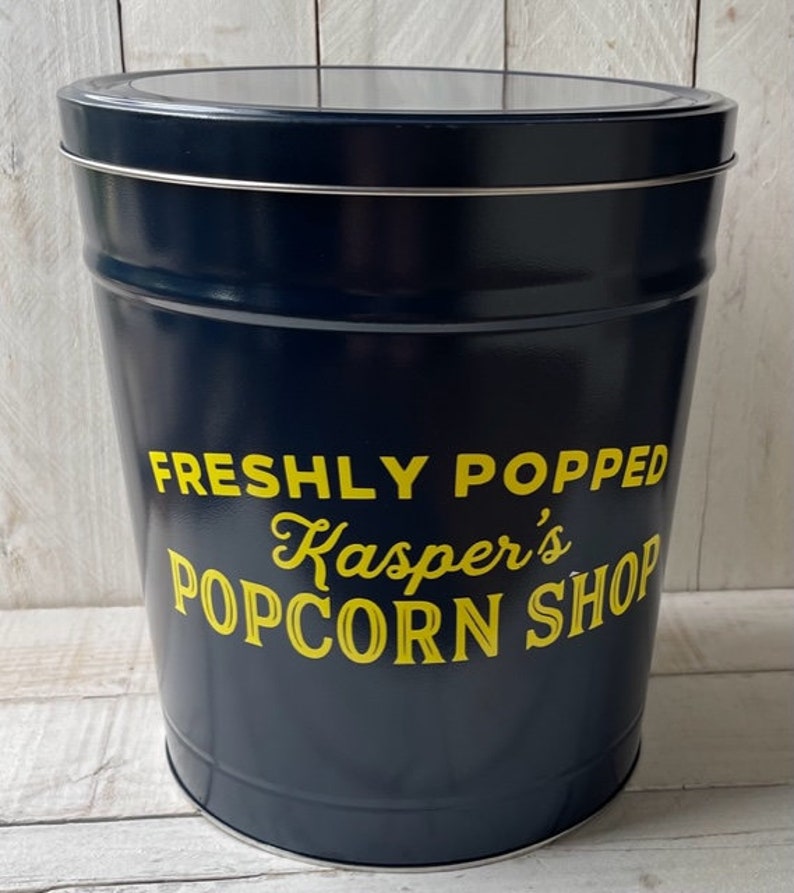 May include: A blue metal popcorn tin with a yellow label that reads "Freshly Popped Kasper's Popcorn Shop".