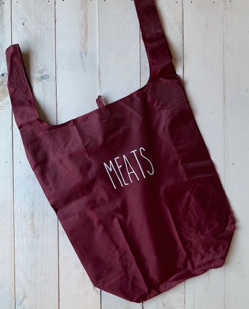 May include: A burgundy reusable shopping bag with the word "MEATS" printed in white on the front.