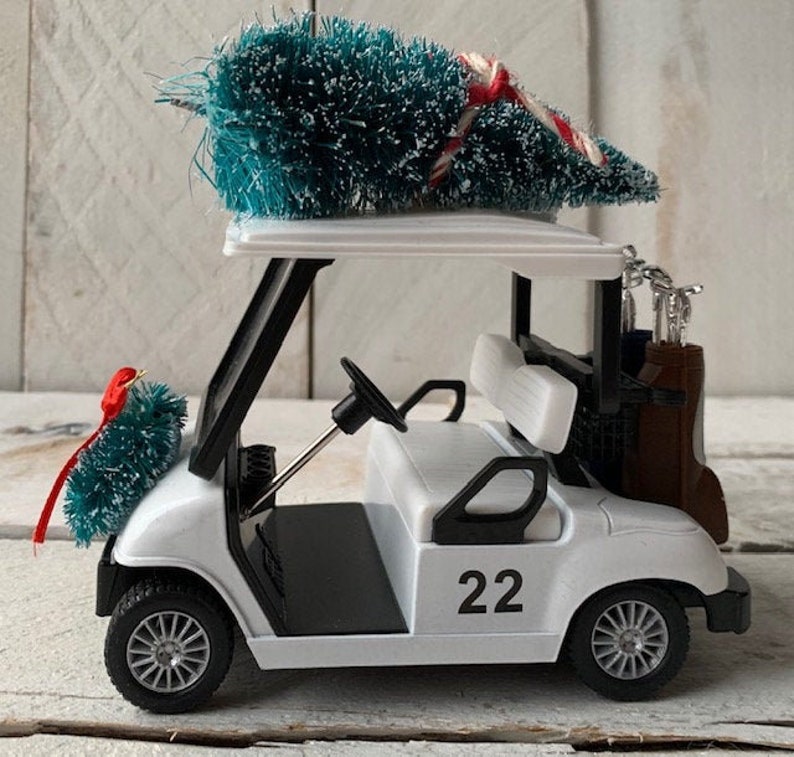 May include: White golf cart with a green Christmas tree on top. The cart has a black steering wheel, black seats, and a black frame. The cart has the number 22 on the side.