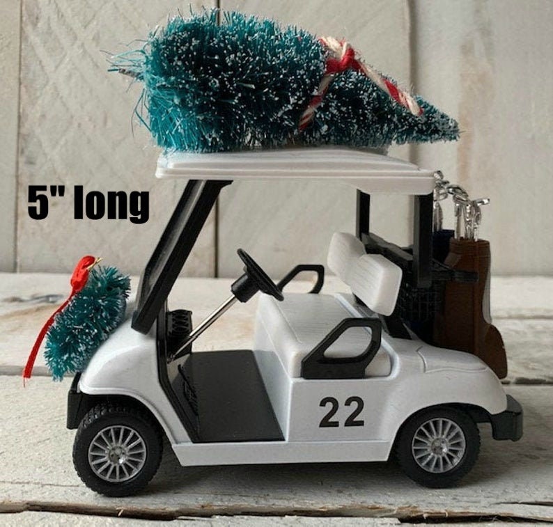 May include: White golf cart with a small Christmas tree on top. The cart has a black steering wheel, black seats, and a black frame. The cart has a number "22" on the side. The tree is 5 inches long.