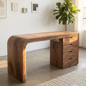 May include: A dark brown wooden desk with a curved waterfall edge on the left side and a four-drawer cabinet on the right. The desk features a built-in light strip along the inner curve and a small integrated power port on the side of the cabinet.