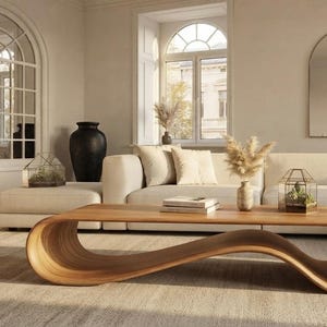 May include: A low-profile coffee table crafted from light-toned wood, featuring a continuous, fluid, wave-like structure that curves to form both the tabletop surface and the base. The design showcases a smooth, natural wood grain finish.