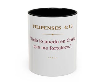 May include: A white ceramic mug with a black interior and rim. The exterior features the text FILIPENSES 4:13 in gold, followed by the Spanish quote "Todo lo puedo en Cristo que me fortalece." in dark red, with decorative gold lines.