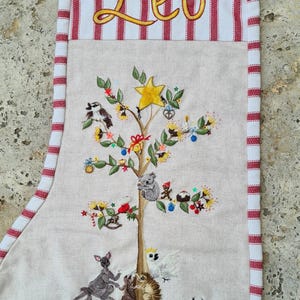 May include: A beige fabric Christmas stocking with red and white striped trim. The name Leo is embroidered in yellow at the top. The center features an embroidered tree with a yellow star, a koala, and various Australian animals at the base.