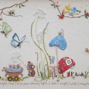 May include: Embroidered artwork featuring a whimsical garden scene with butterflies, flowers, and mushrooms. A fairy plays a horn, and mice are in a cart. The text reads, "Sun beams shining bright, how I love your shining light. I wish I might, I wish I may have the wish I wish today."