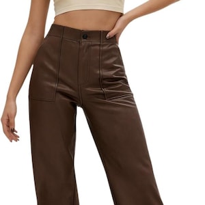 Può includere: Un top corto senza maniche color beige con girocollo abbinato a pantaloni a vita alta in similpelle marrone scuro, caratterizzati da chiusura con bottone, cuciture verticali e due tasche frontali applicate.