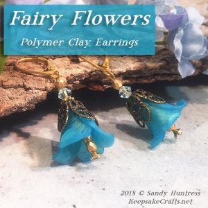 May include: A pair of blue polymer clay fairy flower earrings with gold accents and crystal beads. The earrings are hanging from gold hooks.