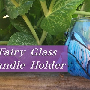 Puede incluir: Un portavelas de vidrio azul con forma de flor con un diseño azul verdoso y morado. El portavelas está encendido y la llama es visible. El texto "Fairy Glass Candle Holder" se muestra sobre un fondo morado.