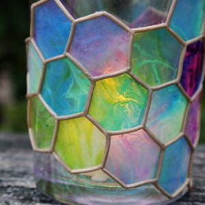 May include: A glass candle holder with a honeycomb design. The glass is painted with swirls of blue, green, yellow, and pink.