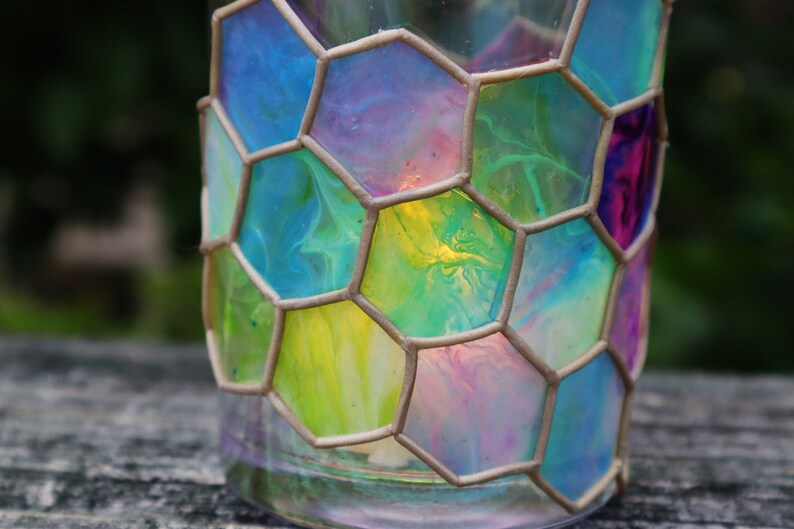 May include: A glass candle holder with a honeycomb design. The glass is painted with swirls of blue, green, yellow, and pink.