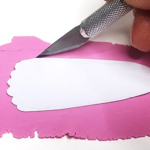 Puede incluir: Una persona utiliza un cuchillo de manualidades para cortar una forma blanca de arcilla de modelar rosa.