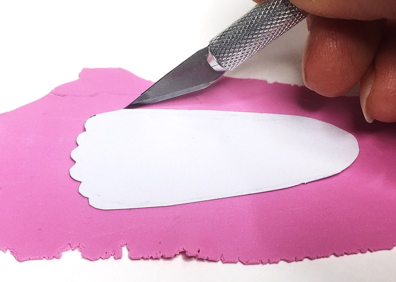 Puede incluir: Una persona utiliza un cuchillo de manualidades para cortar una forma blanca de arcilla de modelar rosa.