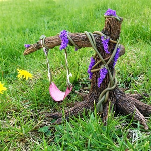 Puede incluir: Un &aacute;rbol en miniatura con un columpio rosa colgando de sus ramas. El &aacute;rbol est&aacute; hecho de madera marr&oacute;n y tiene flores moradas que crecen en &eacute;l. El &aacute;rbol est&aacute; situado sobre un fondo de hierba verde.