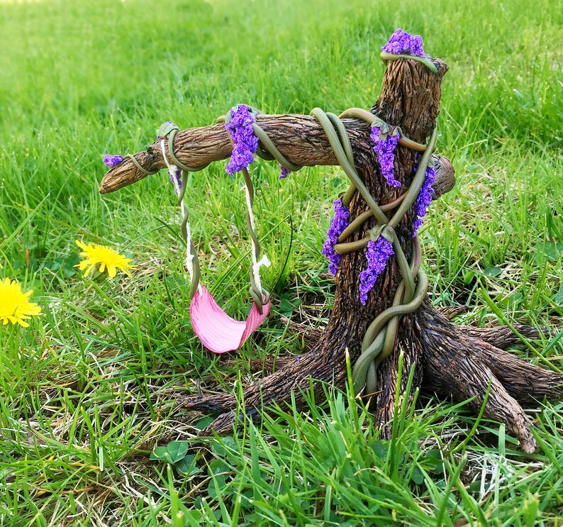 Puede incluir: Un &aacute;rbol en miniatura con un columpio rosa colgando de sus ramas. El &aacute;rbol est&aacute; hecho de madera marr&oacute;n y tiene flores moradas que crecen en &eacute;l. El &aacute;rbol est&aacute; situado sobre un fondo de hierba verde.