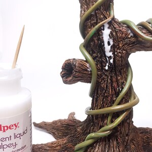 Puede incluir: Primer plano de un tronco de &aacute;rbol con enredaderas verdes envueltas a su alrededor. Se est&aacute; aplicando pegamento blanco a las enredaderas para asegurarlas al tronco.