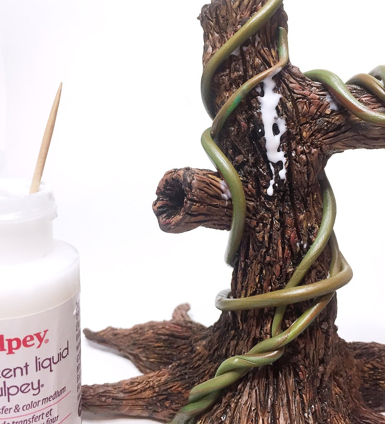 Puede incluir: Primer plano de un tronco de &aacute;rbol con enredaderas verdes envueltas a su alrededor. Se est&aacute; aplicando pegamento blanco a las enredaderas para asegurarlas al tronco.