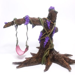 Puede incluir: Un &aacute;rbol en miniatura con un columpio rosa colgando de las ramas. El &aacute;rbol est&aacute; hecho de arcilla marr&oacute;n y tiene enredaderas verdes envueltas a su alrededor. El &aacute;rbol est&aacute; decorado con flores moradas.