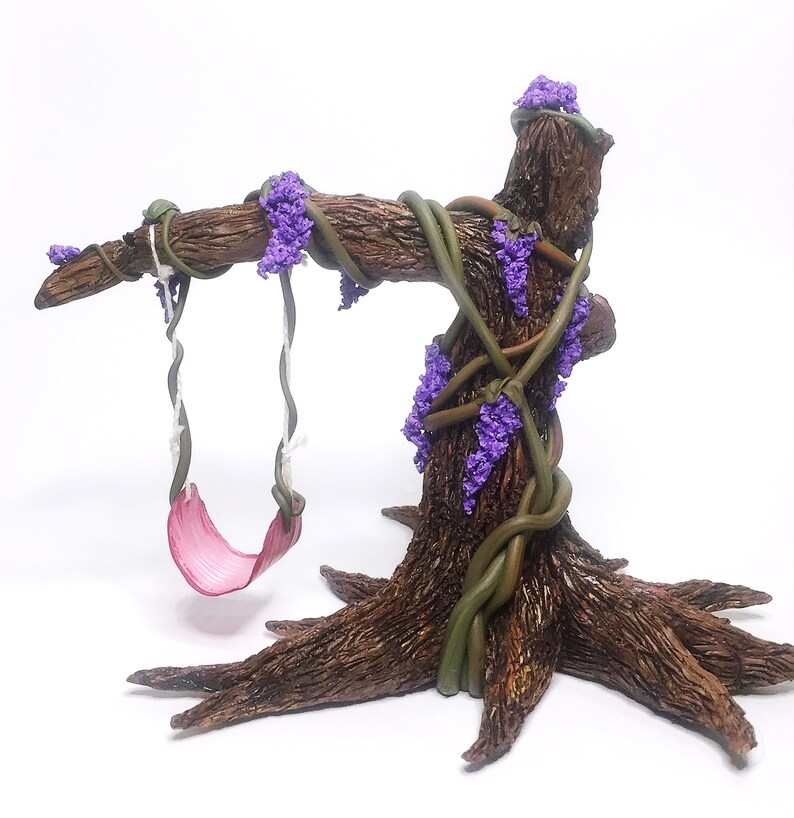 Puede incluir: Un &aacute;rbol en miniatura con un columpio rosa colgando de las ramas. El &aacute;rbol est&aacute; hecho de arcilla marr&oacute;n y tiene enredaderas verdes envueltas a su alrededor. El &aacute;rbol est&aacute; decorado con flores moradas.