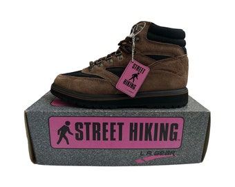 May include: Brown and black hiking boot with a matching box. The boot has a suede-like texture, metal eyelets, and a black collar. A pink tag reads "Street Hiking". The box features the words "Street Hiking" in pink.