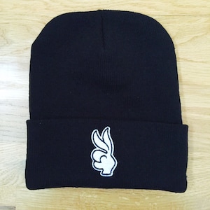 Peut inclure: Un bonnet noir avec un signe OK brodé en blanc.