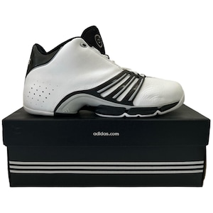 Puede incluir: Zapatillas de baloncesto Adidas blancas y negras con una caja negra que dice "adidas.com".