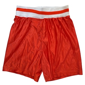 May include: Bright orange mesh shorts with a white and orange striped waistband. The shorts are made of a lightweight, breathable material, perfect for athletic activities or casual wear.