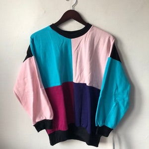 May include: A multi-colored sweatshirt with a patchwork design. The sweatshirt is made of a soft, comfortable fabric and features a crew neck and long sleeves. The colors are pink, blue, purple, and black.
