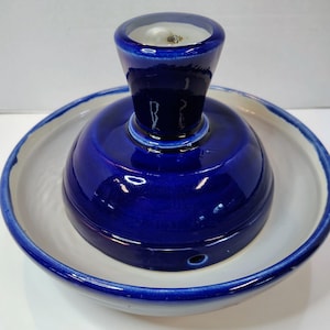 Könnte beinhalten: Ein Keramik-Butterdose mit einer tiefblauen Kobaltglasur auf der Außenseite und einem strahlend weißen Inneren. Die Basis ist eine breite, flache Schale, während der obere Teil ein glockenförmiger Deckel mit einem zentralen Griff ist.