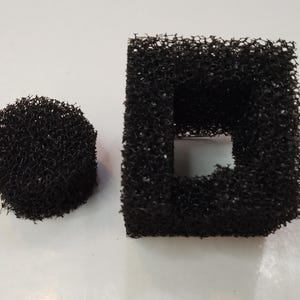 Puede incluir: Dos filtros de espuma negros, uno redondo y otro cuadrado con una abertura rectangular en el centro.