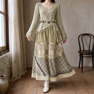 Puede incluir: Una blusa de manga larga color verde salvia con cuello en V, patrón de ganchillo y ribete de borlas, combinada con una falda larga superpuesta con una sección de patchwork floral, una sección a cuadros y un dobladillo de encaje crema.