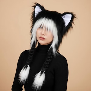 May include: A black and white faux fur hat featuring prominent animal ears with white inner detailing. The hat includes long, straight white bangs and two thick, braided black hair extensions that hang down, each ending in a fluffy white and black tip.