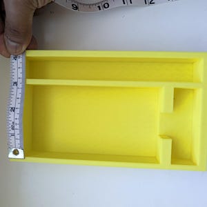 May include: A bright yellow rectangular organiser tray with multiple interior compartments. A white measuring tape is positioned along the left side, indicating a width of approximately 10 cm for the tray's side wall.