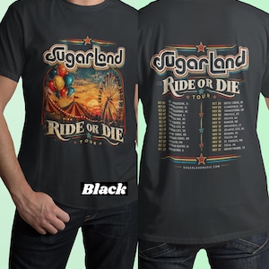 May include: A black short-sleeve t-shirt featuring a graphic print of a carnival scene with a ferris wheel, circus tent, and balloons. The front displays the text Sugarland Ride or Die Tour. The back lists tour dates and locations.